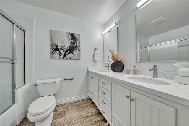 full bathroom featuring a textured ceiling, toilet, vanity, and combined bath / shower with glass door