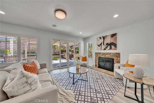 living room with french doors, plenty of natural light, a stone fireplace, and light hardwood / wood-style flooring