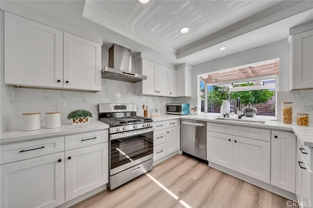 kitchen featuring white cabinetry, appliances with stainless steel finishes, wall chimney range hood, light hardwood / wood-style flooring, and sink