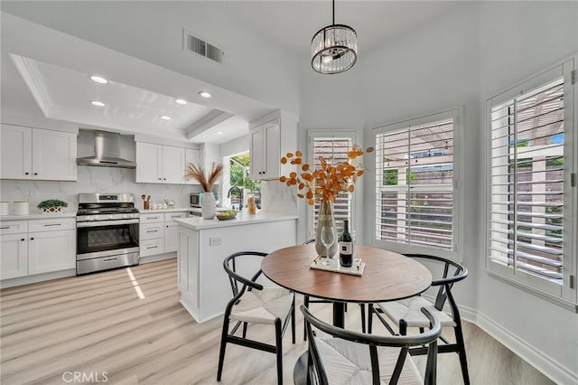 kitchen featuring pendant lighting, a raised ceiling, white cabinetry, appliances with stainless steel finishes, and wall chimney exhaust hood