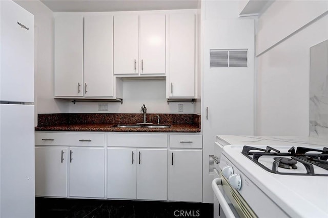 kitchen featuring dark stone counters, sink, white appliances, and white cabinetry