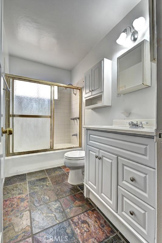 full bathroom featuring toilet, bath / shower combo with glass door, and vanity