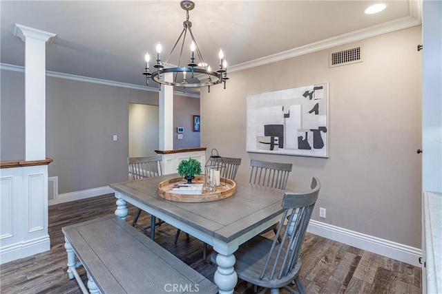 dining area featuring dark wood-type flooring, ornate columns, crown molding, and a notable chandelier