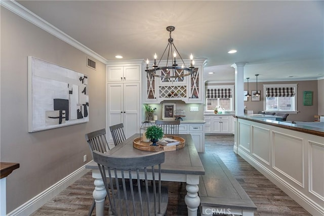 dining room featuring dark hardwood / wood-style flooring, ornamental molding, a chandelier, and decorative columns