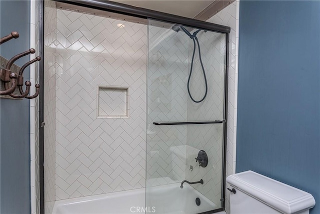 bathroom featuring combined bath / shower with glass door and toilet