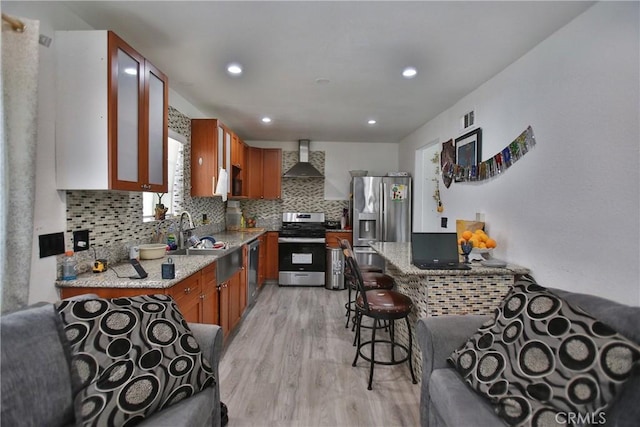 kitchen featuring light stone countertops, appliances with stainless steel finishes, wall chimney exhaust hood, and light wood-type flooring