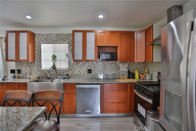 kitchen featuring light stone counters, backsplash, appliances with stainless steel finishes, and light wood-type flooring