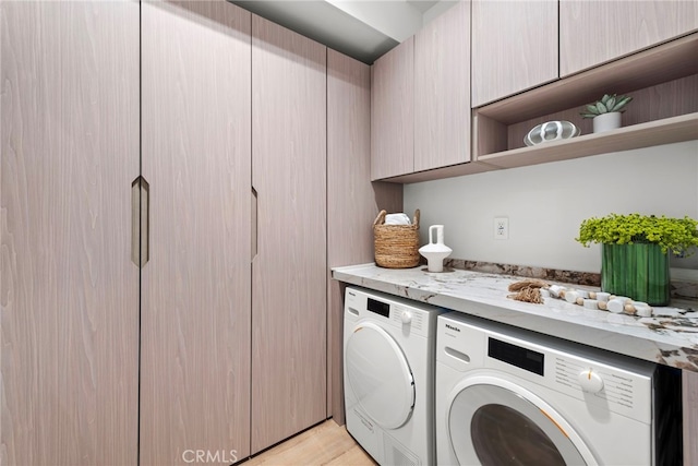 laundry area featuring cabinet space, light wood-style flooring, and washing machine and clothes dryer