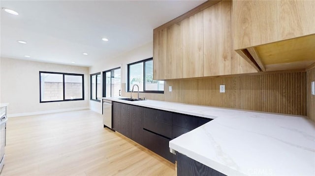 kitchen with light brown cabinets, stainless steel dishwasher, light stone counters, and light hardwood / wood-style floors