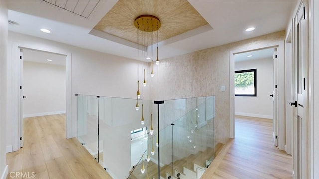 hallway featuring a tray ceiling and light hardwood / wood-style flooring