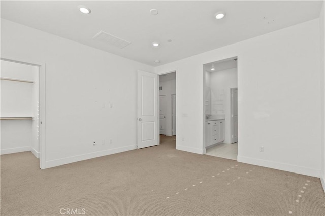 unfurnished bedroom with a spacious closet, light colored carpet, and connected bathroom