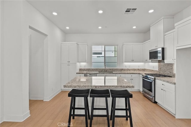 kitchen with light stone counters, appliances with stainless steel finishes, white cabinets, and a kitchen island