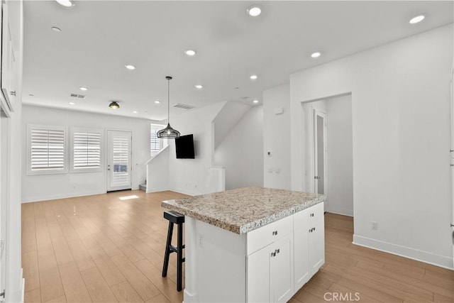 kitchen with pendant lighting, a kitchen island, white cabinetry, light hardwood / wood-style floors, and a breakfast bar area