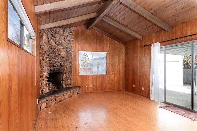 unfurnished living room featuring a stone fireplace, wood walls, lofted ceiling with beams, light hardwood / wood-style floors, and wooden ceiling