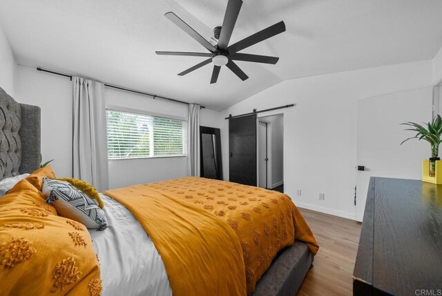 bedroom with light wood-type flooring, ceiling fan, vaulted ceiling, and a barn door