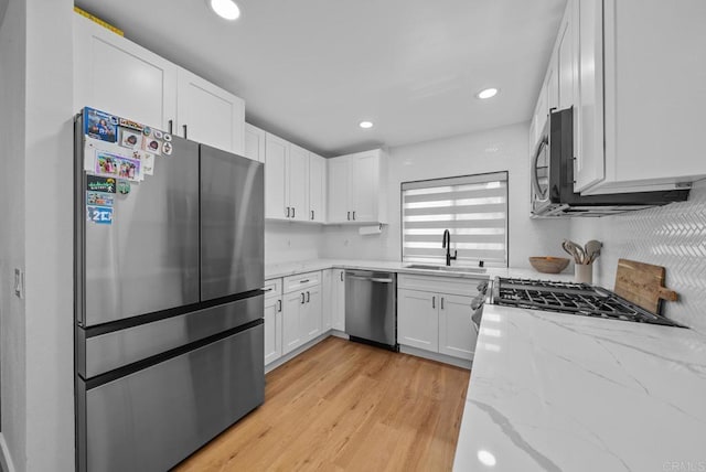 kitchen with appliances with stainless steel finishes, white cabinetry, light hardwood / wood-style floors, sink, and light stone counters