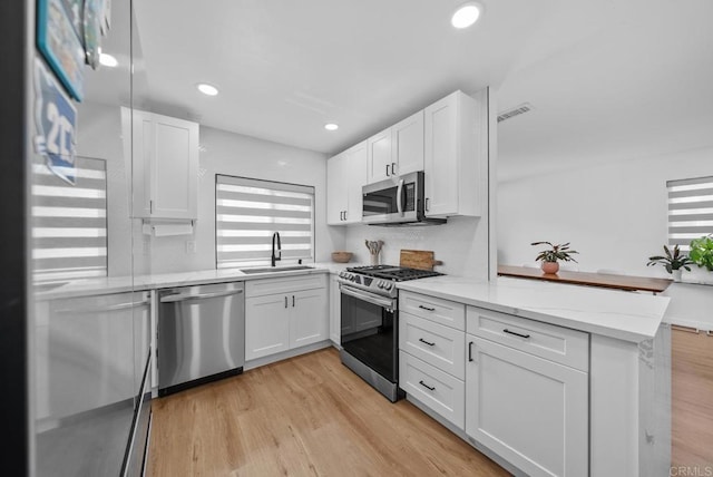 kitchen featuring appliances with stainless steel finishes, white cabinetry, light hardwood / wood-style floors, sink, and kitchen peninsula