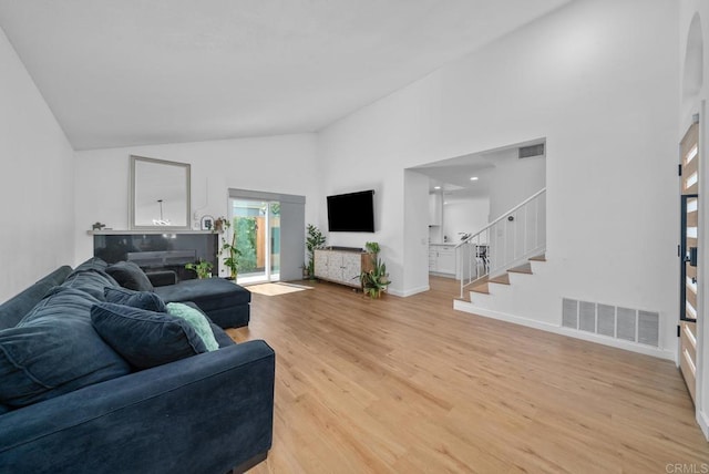 living room featuring high vaulted ceiling, a fireplace, and light hardwood / wood-style floors