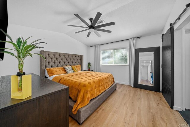 bedroom featuring ceiling fan, vaulted ceiling, a barn door, and light wood-type flooring