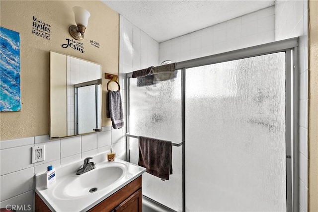 bathroom featuring a shower with door, decorative backsplash, tile walls, a textured ceiling, and vanity