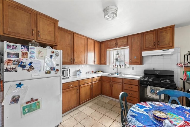 kitchen featuring light tile patterned floors, decorative backsplash, black range with gas cooktop, white refrigerator, and sink