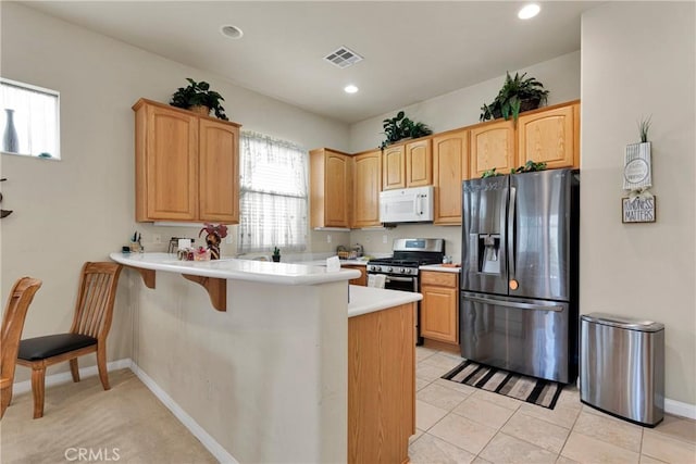 kitchen with light tile patterned flooring, appliances with stainless steel finishes, a kitchen bar, and kitchen peninsula