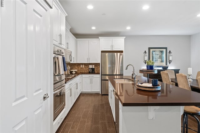 kitchen with a center island with sink, a breakfast bar, sink, white cabinetry, and appliances with stainless steel finishes