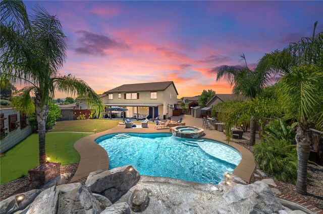 pool at dusk with a yard, a patio, and an in ground hot tub