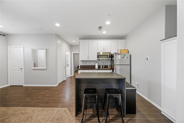 kitchen with white cabinetry, a breakfast bar area, appliances with stainless steel finishes, a center island, and sink