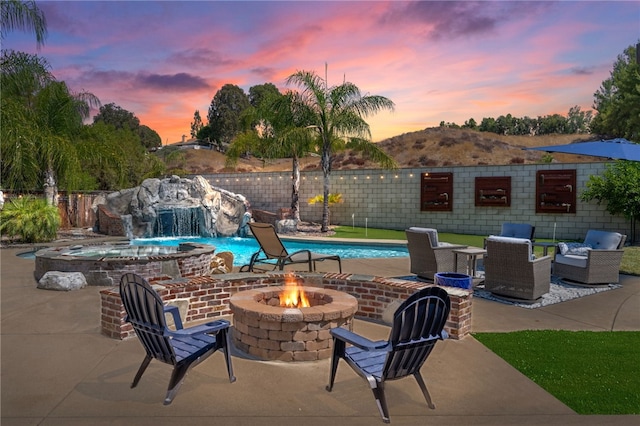 patio terrace at dusk featuring pool water feature and a fire pit