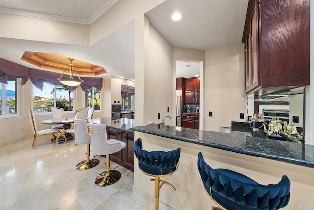 kitchen with decorative light fixtures, dark stone counters, kitchen peninsula, a breakfast bar, and a tray ceiling