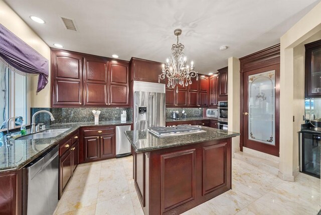 kitchen featuring stainless steel appliances, a kitchen island, decorative light fixtures, a chandelier, and sink