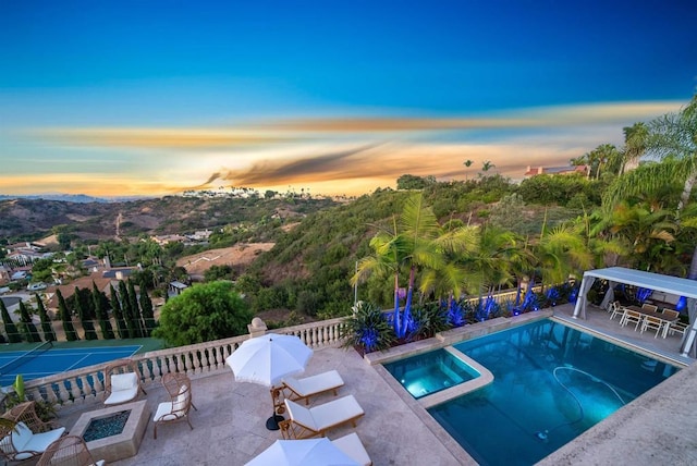 pool at dusk with a patio area and a fire pit