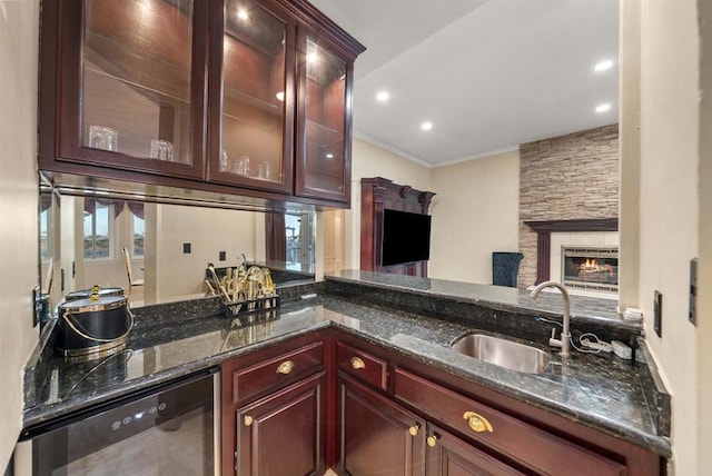 kitchen with a fireplace, sink, dark stone countertops, and ornamental molding