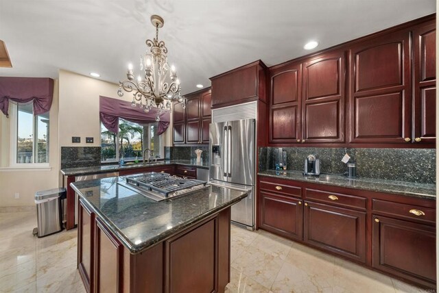 kitchen with pendant lighting, a kitchen island, appliances with stainless steel finishes, dark stone counters, and a chandelier