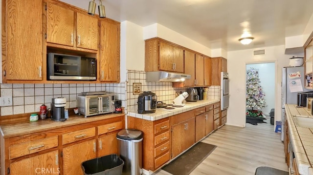 kitchen with backsplash, tile countertops, stainless steel appliances, and light hardwood / wood-style floors