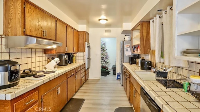 kitchen featuring backsplash, light hardwood / wood-style flooring, tile counters, and stainless steel appliances