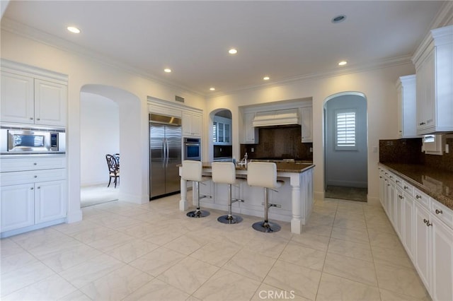 kitchen with a kitchen breakfast bar, white cabinetry, tasteful backsplash, and built in appliances