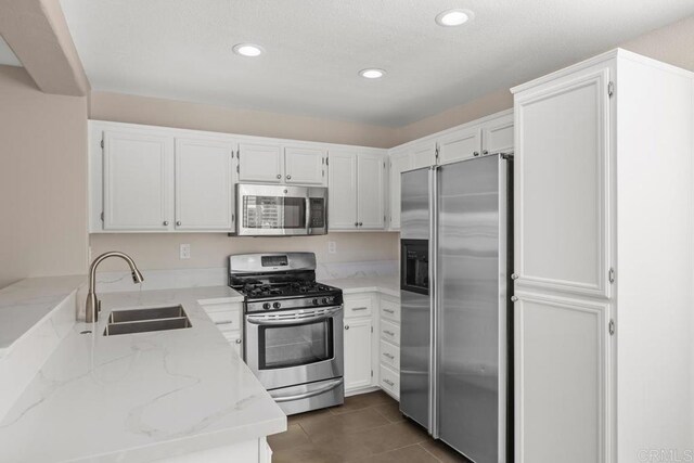 kitchen with stainless steel appliances, sink, light stone countertops, white cabinets, and dark tile patterned floors