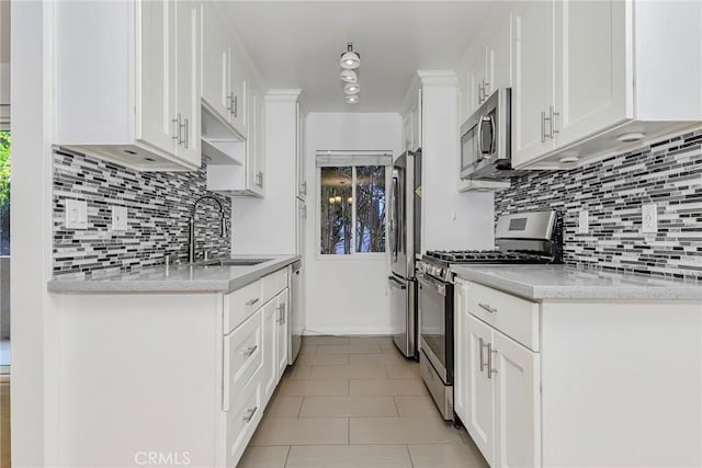 kitchen with appliances with stainless steel finishes, white cabinetry, sink, light stone counters, and light tile patterned floors