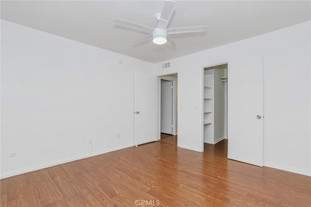 unfurnished bedroom with ceiling fan, wood-type flooring, a spacious closet, and a closet