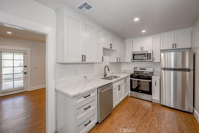 kitchen with white cabinets, appliances with stainless steel finishes, light hardwood / wood-style floors, sink, and light stone counters