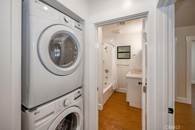 laundry room featuring stacked washer / dryer, sink, and hardwood / wood-style floors