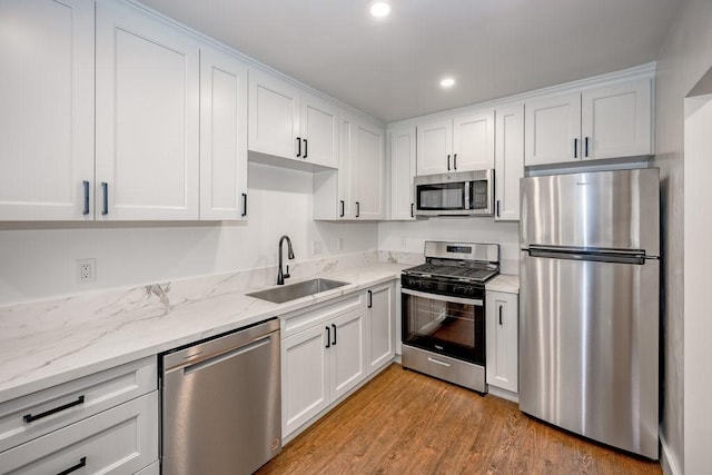 kitchen with sink, white cabinetry, light hardwood / wood-style flooring, appliances with stainless steel finishes, and light stone counters