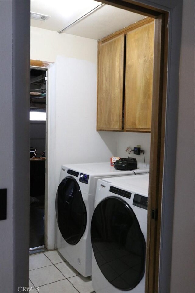 clothes washing area featuring cabinets, light tile patterned floors, and washer and clothes dryer