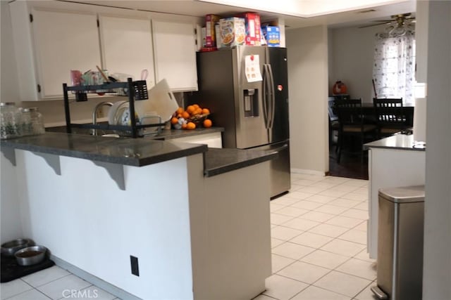 kitchen with a breakfast bar, stainless steel fridge, white cabinets, light tile patterned floors, and kitchen peninsula