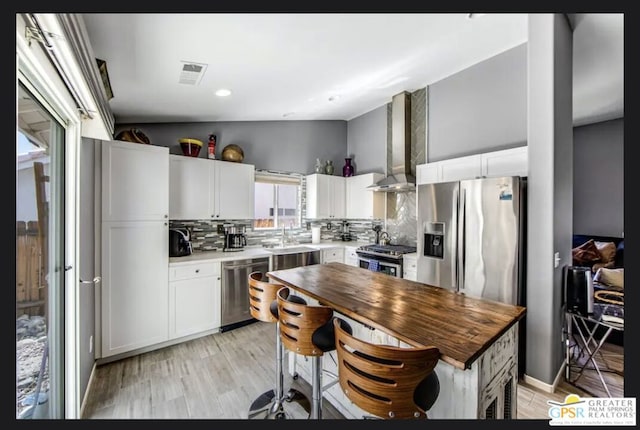 kitchen with white cabinets, backsplash, appliances with stainless steel finishes, and wall chimney exhaust hood