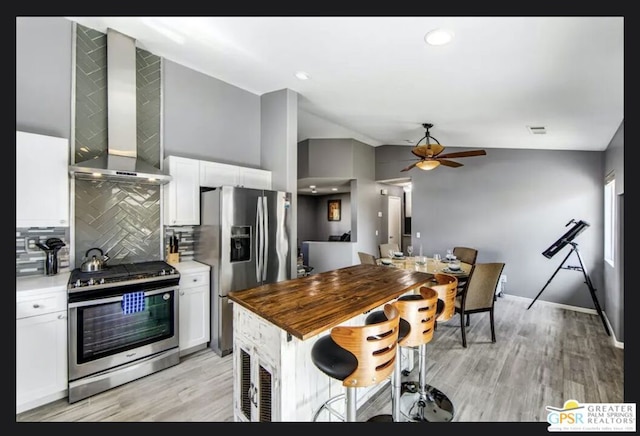 kitchen with backsplash, white cabinetry, light wood-type flooring, appliances with stainless steel finishes, and wall chimney exhaust hood