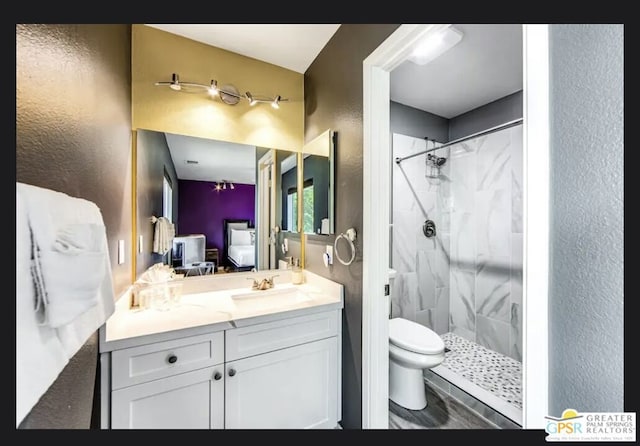 bathroom with vanity, toilet, and tiled shower