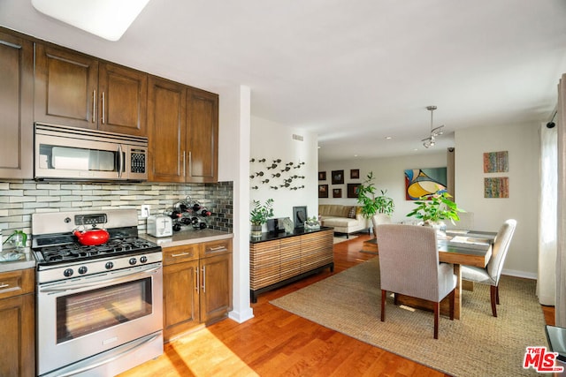 kitchen with appliances with stainless steel finishes, backsplash, light hardwood / wood-style floors, and pendant lighting